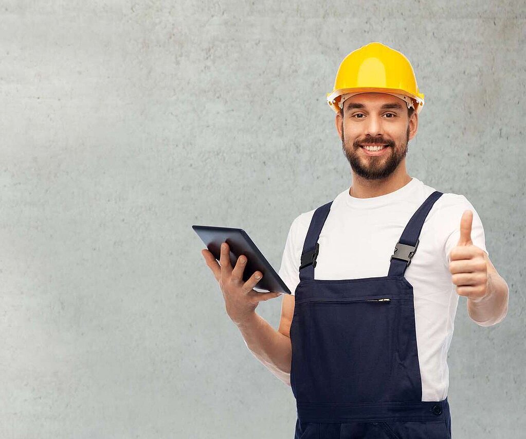 Arbeiter mit gelbem Helm und Blaumann mit Tablet in der Hand